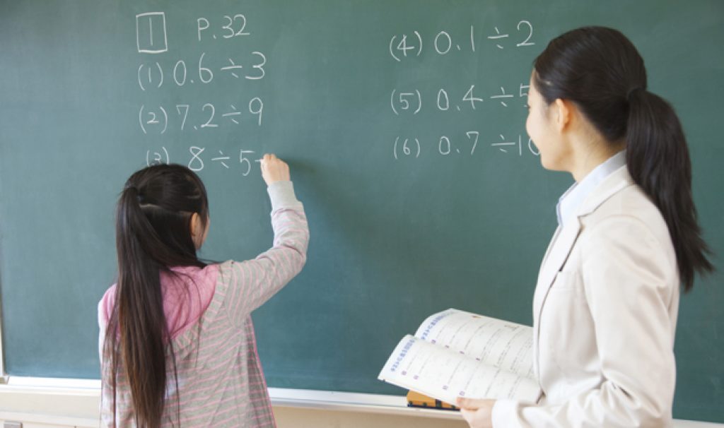 student-solving-math-equation-on-black-board-while-teacher-observes-sum