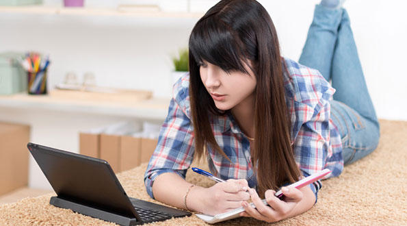 girl-with-fringe-laying-down-on-bench-taking-note-and-studying-on-laptop-in-her-room