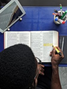 student-using-yellow-highlighter-on-text-book-at-table-with-stationary-and-tab